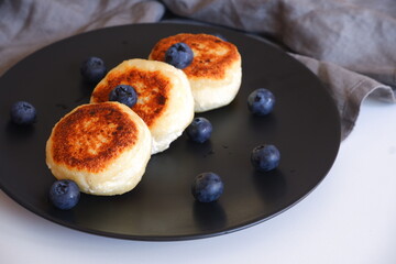 Curd pancakes with blueberries on a black plate.