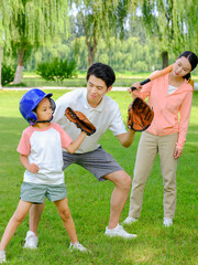 Happy family of three playing baseball in the park