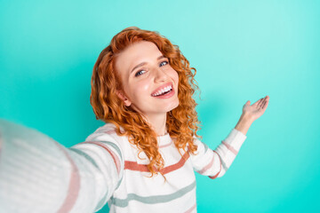 Photo portrait of red haired girl in striped sweater smiling taking selfie showing empty space isolated vivid teal color background