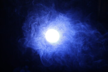 Artificial magic smoke in blue light on black background