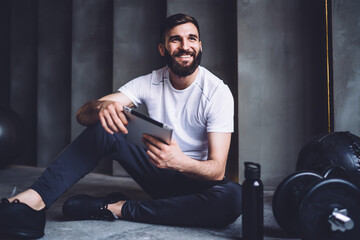 Cheerful caucasian male in activewear using modern digital tablet for blogging and share media...