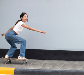 Asian young woman playing surfskate or skate board isolated on gray background at urban city...