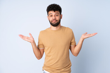 Young Moroccan man isolated on blue background making doubts gesture