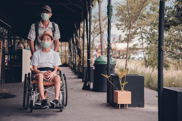 Obraz premium Asian special child on wheelchair wearing mask protection flu Covid 19 or Coronavirus,Wear N95 or cotton masks when to do outdoor activities,New normal to prevent the spread of the virus disease.