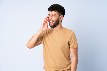 Young Moroccan man isolated on blue background shouting with mouth wide open to the side