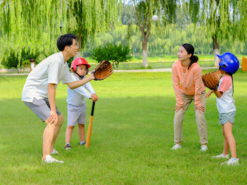 Happy family of four playing baseball in the park
