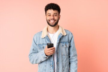 Young Moroccan man using mobile phone isolated on pink background with surprise facial expression