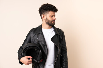 Fototapeta premium Young Moroccan man with a motorcycle helmet isolated on beige background looking to the side