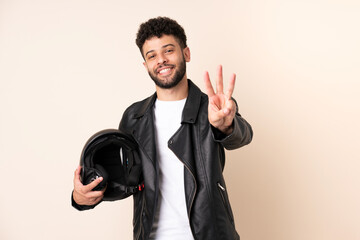 Fototapeta premium Young Moroccan man with a motorcycle helmet isolated on beige background happy and counting three with fingers