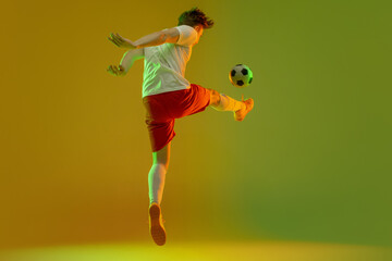 Young caucasian man, male soccer football player training isolated on gradient blue pink background in neon light