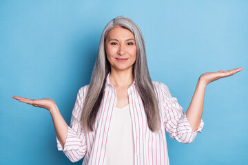 Photo of cheerful nice positive old woman hold hands empty space scales isolated on blue color background