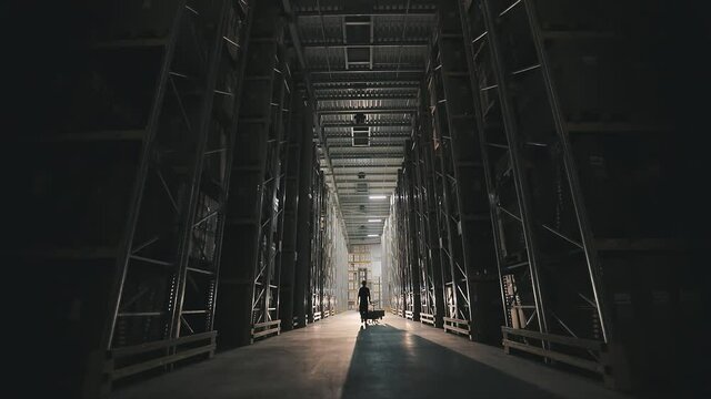 Turning on lighting in a factory warehouse. Morning in the factory, a man walks through the warehouse light turns on
