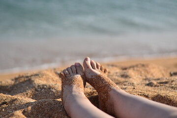 Close-up feet in the sand. Sunny weather on a sandy beach. Vacation at sea. Getting a tan in the sun.