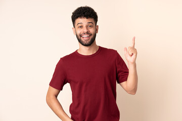 Fototapeta premium Young Moroccan man isolated on beige background thinking an idea pointing the finger up