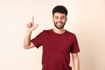 Naklejka premium Young Moroccan man isolated on beige background pointing up a great idea