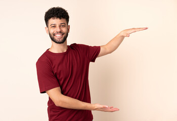 Young Moroccan man isolated on beige background holding copyspace to insert an ad