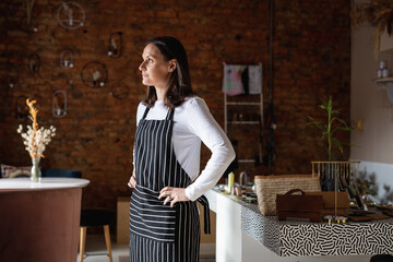 Caucasian female business owner wearing striped apron and looking out of window