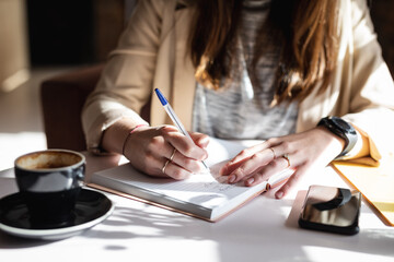 Close up of hands of caucasian female customer sitting at table, making notes