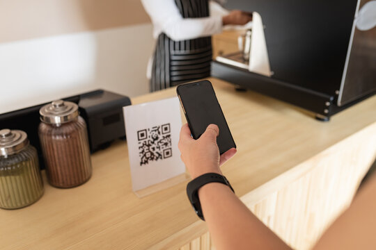 Hand of caucasian female customer standing at countertop, holding smartphone, scanning qr code