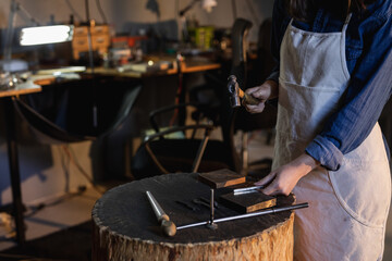 Midsection of caucasian female jeweller holding jewelry tools, making jewelry in workshop