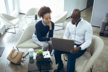 Two diverse male and female business colleagues sitting and using laptop