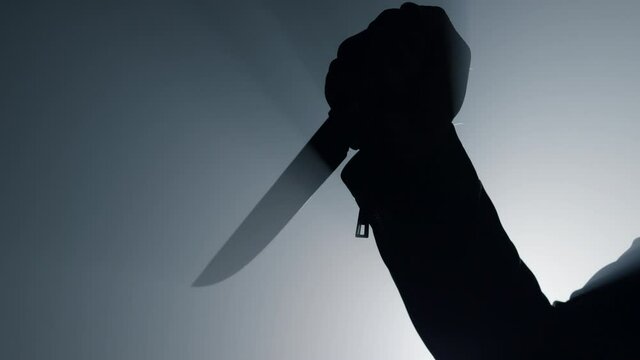 Silhouette man arm holding knife in dark. Criminal hand attacking with dagger. 