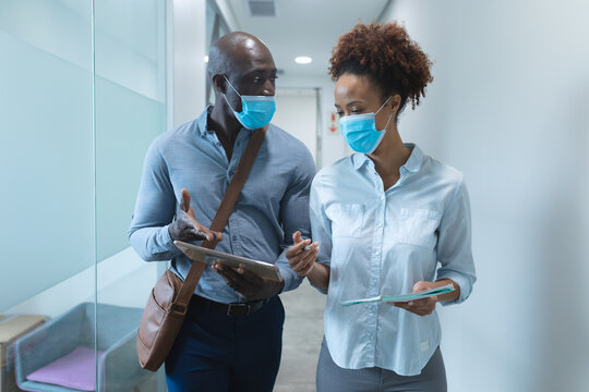 Diverse male and female business colleagues wearing face masks, using tablet and talking - Powered by Adobe