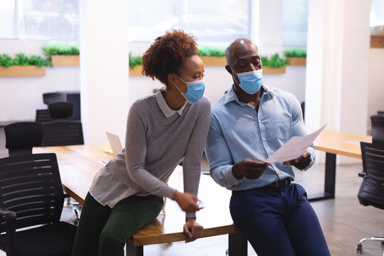 Two diverse male and female business colleagues wearing face masks and holding documents