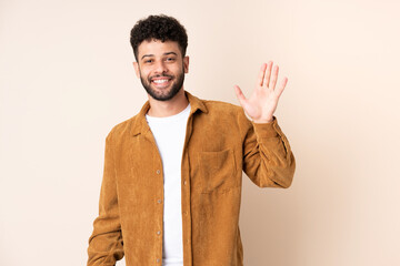 Young Moroccan man isolated on beige background saluting with hand with happy expression