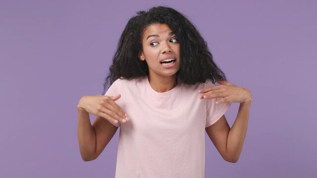 Fun shy shamed african american woman 20s years old wears pink T-shirt look camera spreading hands say oops ouch oh omg i am so sorry isolated on pastel violet purple color background studio portrait