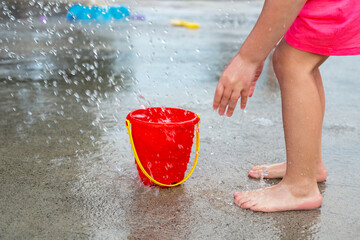 Little girl playing barefoot at water splash pad fountain in the park playground on a hot summer day.
