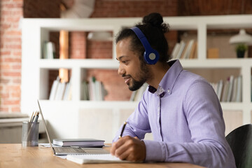 Interested young african american man listening educational lecture, wearing headphones. Motivated mixed race male student improving professional knowledge distantly, studying on online courses.
