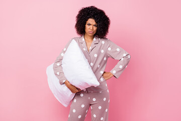 Photo of charming angry curly dark skin woman dotted nightwear holding white pillow isolated pink...