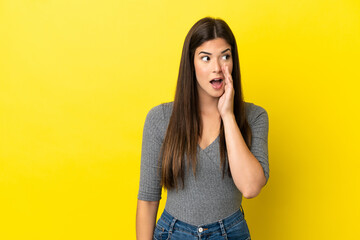 Young Brazilian woman isolated on yellow background whispering something with surprise gesture while looking to the side