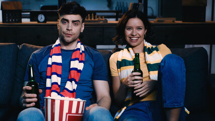 Fototapeta na wymiar displeased man and happy woman sitting with bottles of beer and watching championship.
