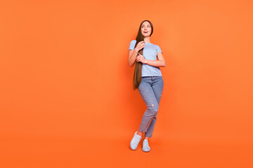 Fototapeta na wymiar Full size photo of young teen girl happy positive smile hands touch hair look empty space isolated over orange color background