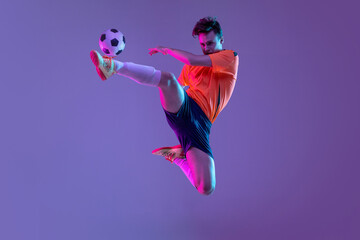 Young caucasian man, male soccer football player training isolated on gradient blue pink background in neon light