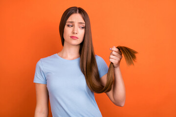 Photo of sad brown hairdo young lady look hair wear blue t-shirt isolated on vivid orange color...