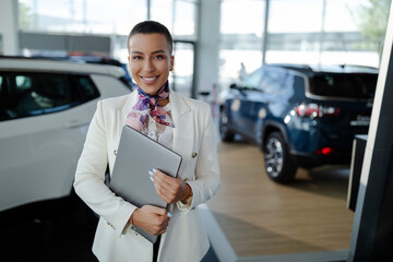 Saleswoman in car showroom holding a laptop computer and selling cars. - obrazy, fototapety, plakaty
