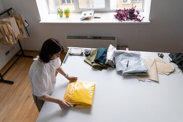 Atelier worker, freelance bespoke sewer in tailoring studio wrap clothes ready for presentation in showroom or retail store. Young girl fashion designer create new cloth collection in workshop studio