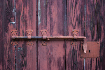 Detail of an ancient red door with a bar.