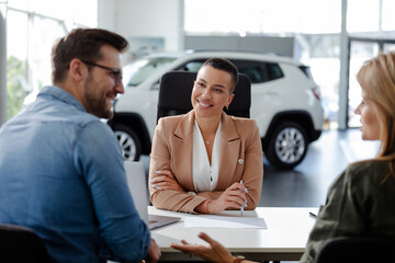 Woman car dealer sitting at the table and talking about car preferences with clients.