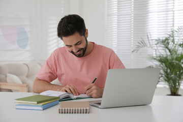 Young man writing down notes during webinar at table in room