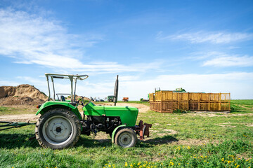 Old green good-looking tractor stands on a farm in a field near agricultural fixtures overlooking the village horizon with blue cloudy sky, on calm spring or summer day.