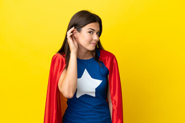Fototapeta na wymiar Super Hero Brazilian woman isolated on yellow background listening to something by putting hand on the ear