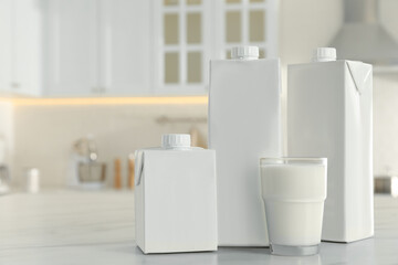 Carton boxes and glass of milk on table in kitchen, space for text