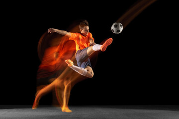 Young caucasian male football or soccer player kicking ball for the goal in mixed light on dark...