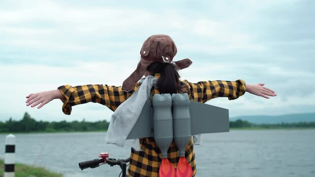 Funny Asian child girl playing with toy rocket sitting on a bicycle and raised arms, Happy kid playing outdoors