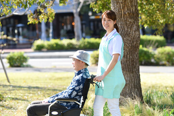 屋外で散歩をする介護ヘルパーの女性と車椅子のシニア男性