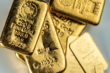 Several cast and minted gold bars on a on grey background. Selective focus.